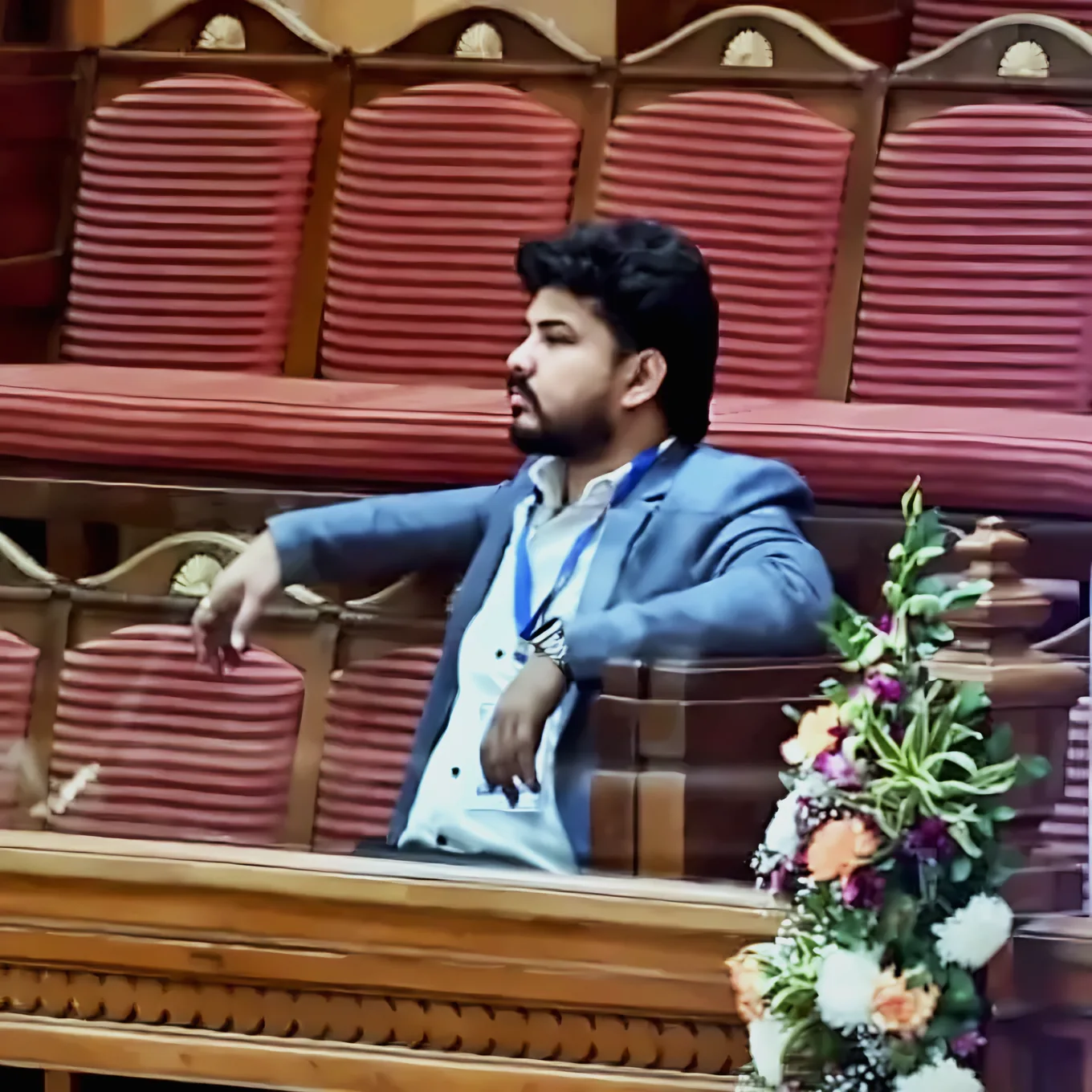 Prem Mishra seated in the visitors’ gallery of a legislative chamber, wearing a delegate lanyard